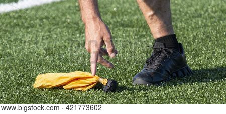 A Game Referees Hand Picking Up The Yellow Penalty Flag That Was Thrown During The Game.