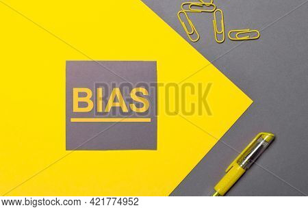 On A Gray And Yellow Background, A Gray Sticker With Yellow Text Bias, Yellow Paper Clips And A Yell