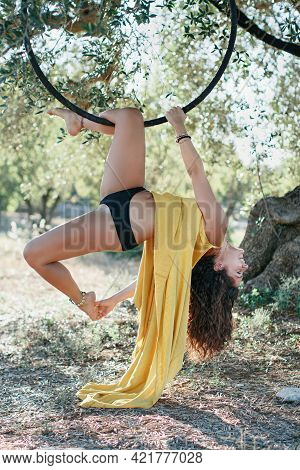 Young Gymnast Woman Posing On A Aeriel Circle In Fron Of The Olive Trees Garden