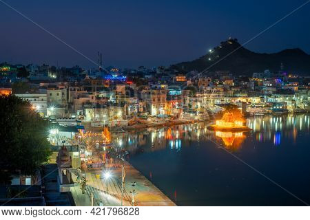 View of famous indian hinduism pilgrimage town sacred holy hindu religious city Pushkar with Brahma temple, aarti ceremony, lake and ghats illuminated at sunset. Rajasthan, India. Horizontal pan