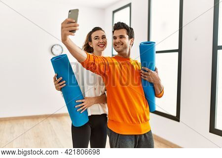 Young hispanic sporty couple holding yoga mat and making selfie by the smartphone at sport center.