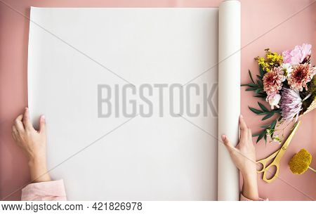 Woman unroll a paper on a pink table by a bouquet of flowers