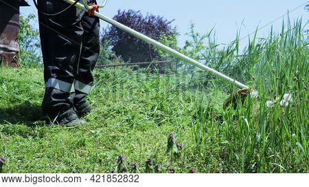 The Legs Of A Grass Mower With A Gasoline Mower While Working, Mowing Tall Grass In A Rustic Atmosph