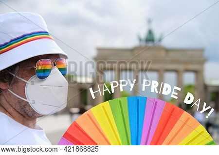 Mature Caucasian Lgbt Man In Berlin With Rainbow Fan And Ribbon On White Summer Hat. Rainbow, Symbol