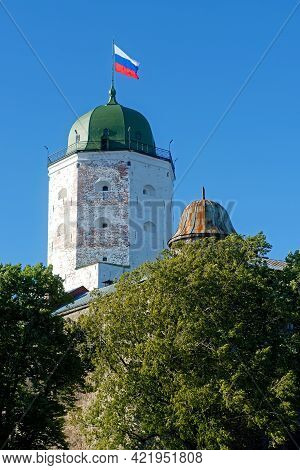 Bashnya Vyborgskogo Zamka S Kupolom I Flagom, Vozvyshayetsya Nad Derev'yami Na Fone Golubogo Neba.