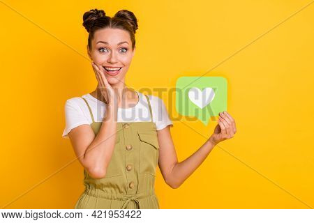 Photo Of Surprised Girl Hold Green Like Card Hand Cheek Open Mouth Wear Green Overall Isolated Yello