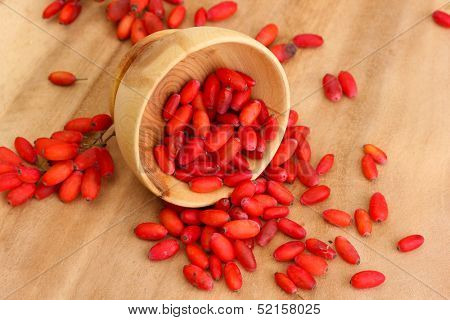 ripe barberries in wooden bowl, on wooden background