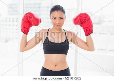 Motivated dark haired model in sportswear wearing red boxing gloves in bright fitness studio