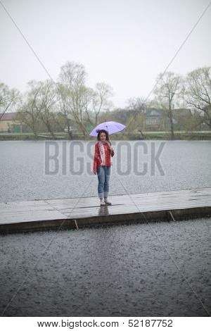 A young woman with a purple umbrella stands on a wooden pier in the rain