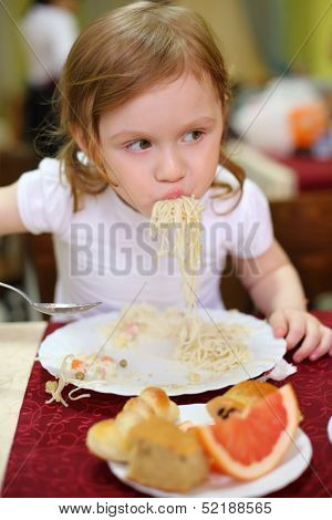 Little girl with pigtails eating spaghetti with a spoon in a cafe