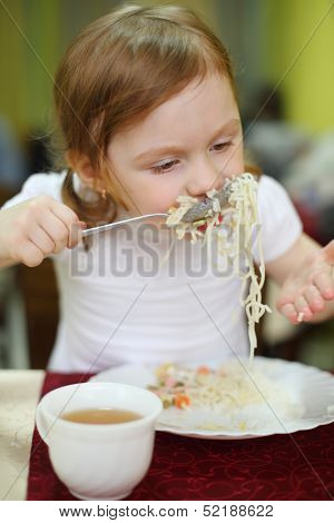 Little girl with pigtails eating spaghetti with a spoon in a cafe