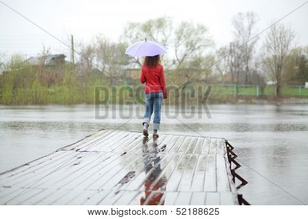 A woman with a purple umbrella stands on a wooden pier, view from the back