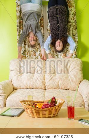 Two women stand upside down and hold on to the sofa