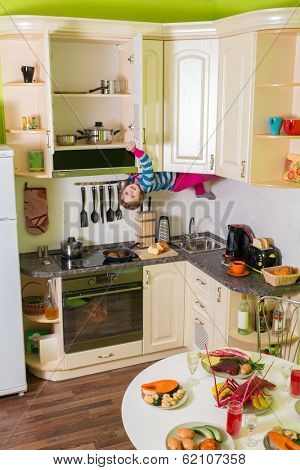 Little girl upside down holds a shelves in the kitchen with table and dishes