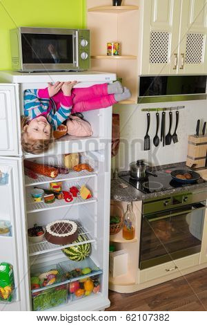 Little girl sits in freezer refrigerator in the kitchen at inverted house