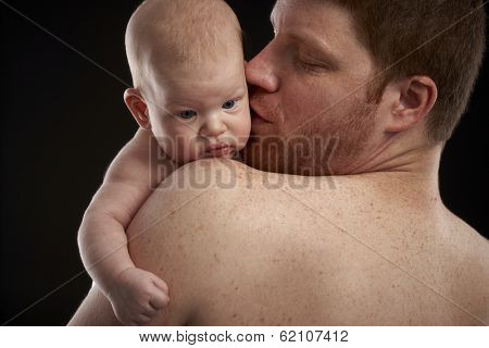Father holding newborn baby, kissing face, semi-nude. Closeup photo.