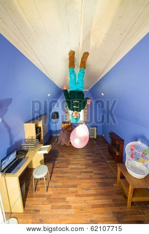 Little boy with air balloon standing on the ceiling in the room