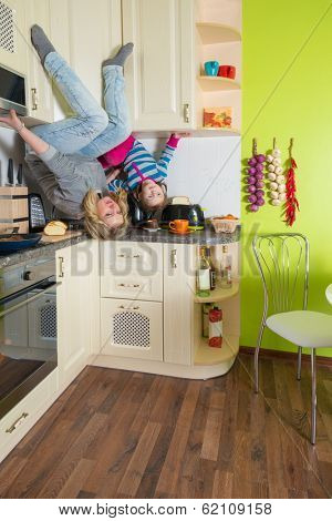 Mother and daughter sitting at shelves upside down in the colored kitchen 