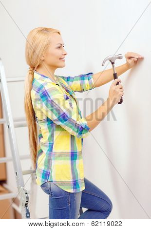 reapir, building and home renovation concept - smiling woman hammering nail in wall