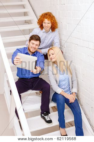 business, technology and startup concept - smiling creative team with tablet pc computer sitting on staircase