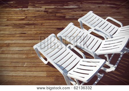 Top view of three empty white deck chairs in a swimming pool deck