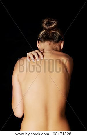 Nude, topless woman, scratching her neck. back view. On black background. 