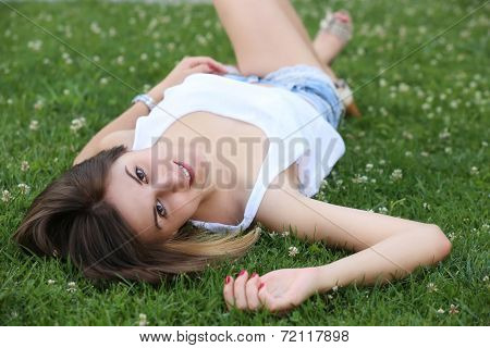 Beautiful, young woman lying on green grass