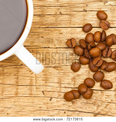 Close Up Of White Ceramic Coffee Cup With Roasted Coffee Beans On Wooden Table - View From Top