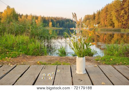 Bright autumn field bouquet of flowers in the hand-made ceramic vase at a bridge on the pond/lake