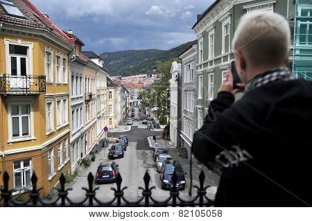 Young girl is taking picture with her phone in the old part of Bergen, Norway