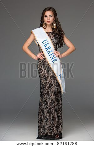 Beautiful young brunette woman with her hair posing in a i long dress. Studio, on gray background