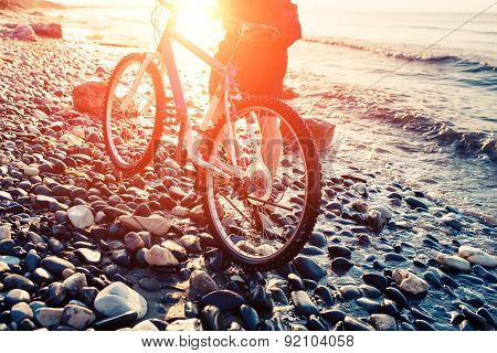 Man with bicycle on a sea shore sunset