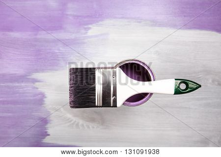 Paintbrush and can with lavender color lying on white wooden background. The surface is half - toned with violette color.