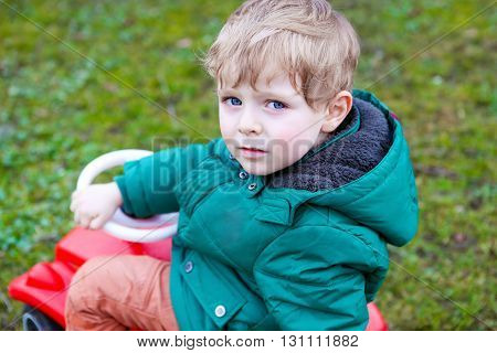 Little todder boy playing with big toy pedal car. Blond happy funny kid having fun on warm spring day.
