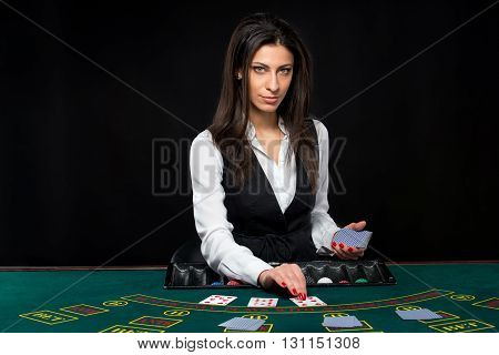 The beautiful girl, dealer, behind a table for game in poker. the dealer deals the cards. He is looking at the camera