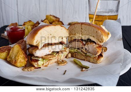 Homemade chicken burger with ketchup, beer and roasted potaoes on wood background.
