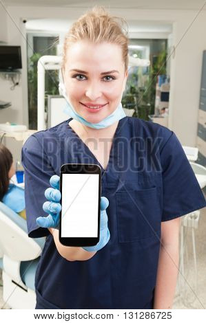 Young attractive dentist holding a smarthphone with blank screen with copyspace in dental office