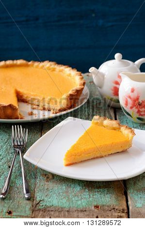 Homemade bright pumpkin pie and teaware on shabby wooden table vertical