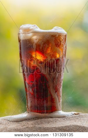 soft drink within glass with ice cubes on sand nature background