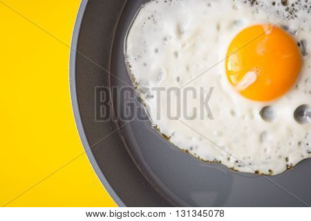 Fried egg on frying pan on yellow background. Top view.