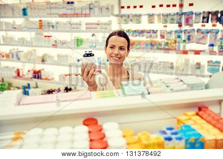 medicine, pharmaceutics, health care and people concept - happy female customer with drug jar at pharmacy