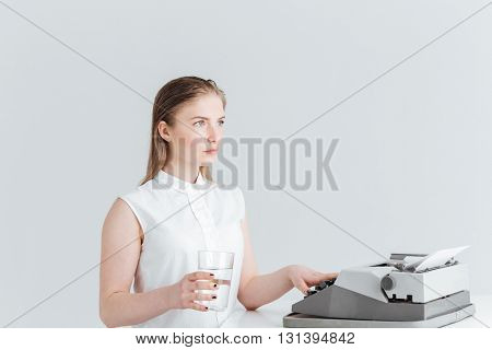 Young woman worrking on retro print machine and holding glass with water isolated on a white background