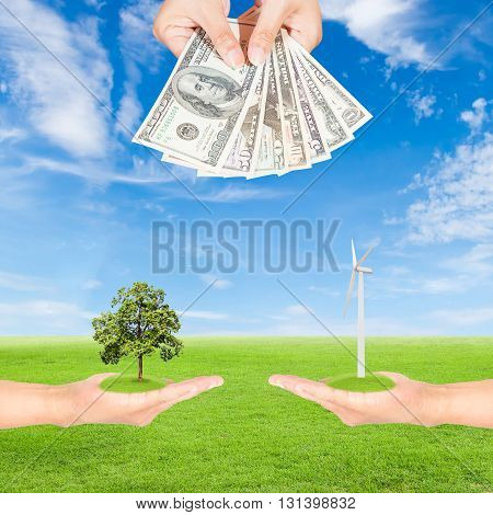 Carbon credits concepthand holding wind turbine with tree and US Dollars banknote against green field and blue sky background