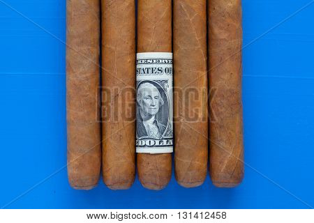 Detail of luxury Cuban cigars with US dollar on the blue desk