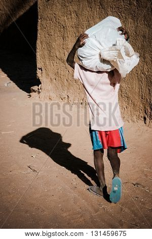 Young african boy carrying a bag on the head, back view