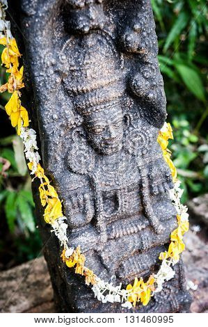 Indian god carved in a black stone rounded with white and yellow flowers, South India