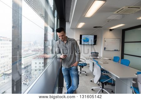 relaxed young businessman using smart phone at modern startup business office meeting room  with big window and city in backgronud