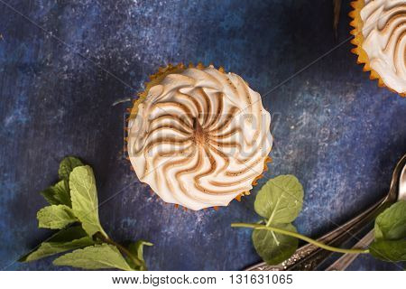 Lemon cupcakes with meringue and mint leaves over blue wooden table. Top view