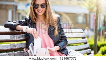 Time to go. Positive and merry young woman packing her books in a bag while sitting on a bench in a park