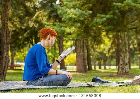 Girl reading a book. /  redheaded girl reading a book on a glade in the park.